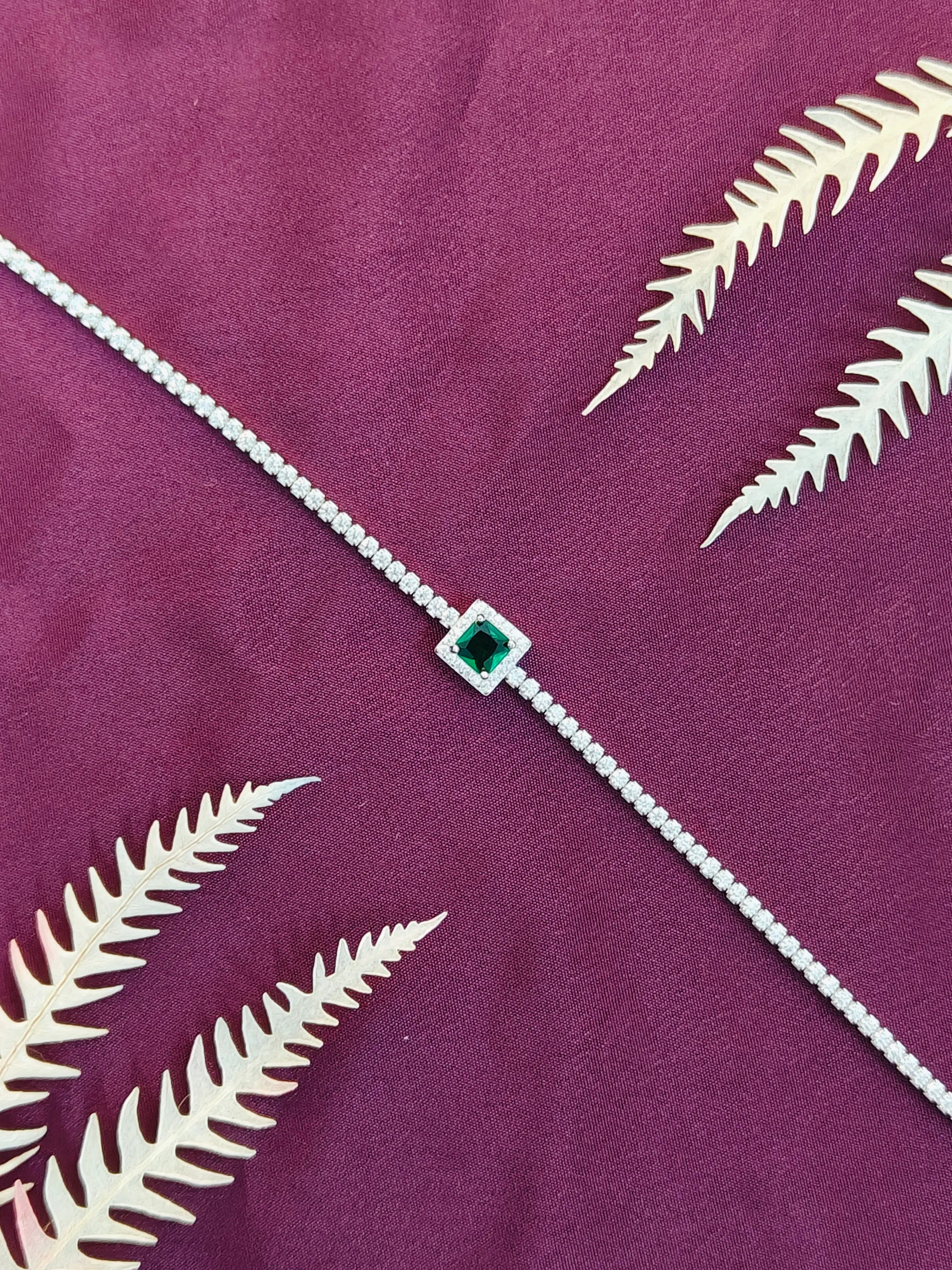 Silver bracelet with a green gemstone on a purple fabric background with white leaf patterns